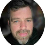 Head shot of white man with short, wavy brown hair and salt and pepper beard and goatee